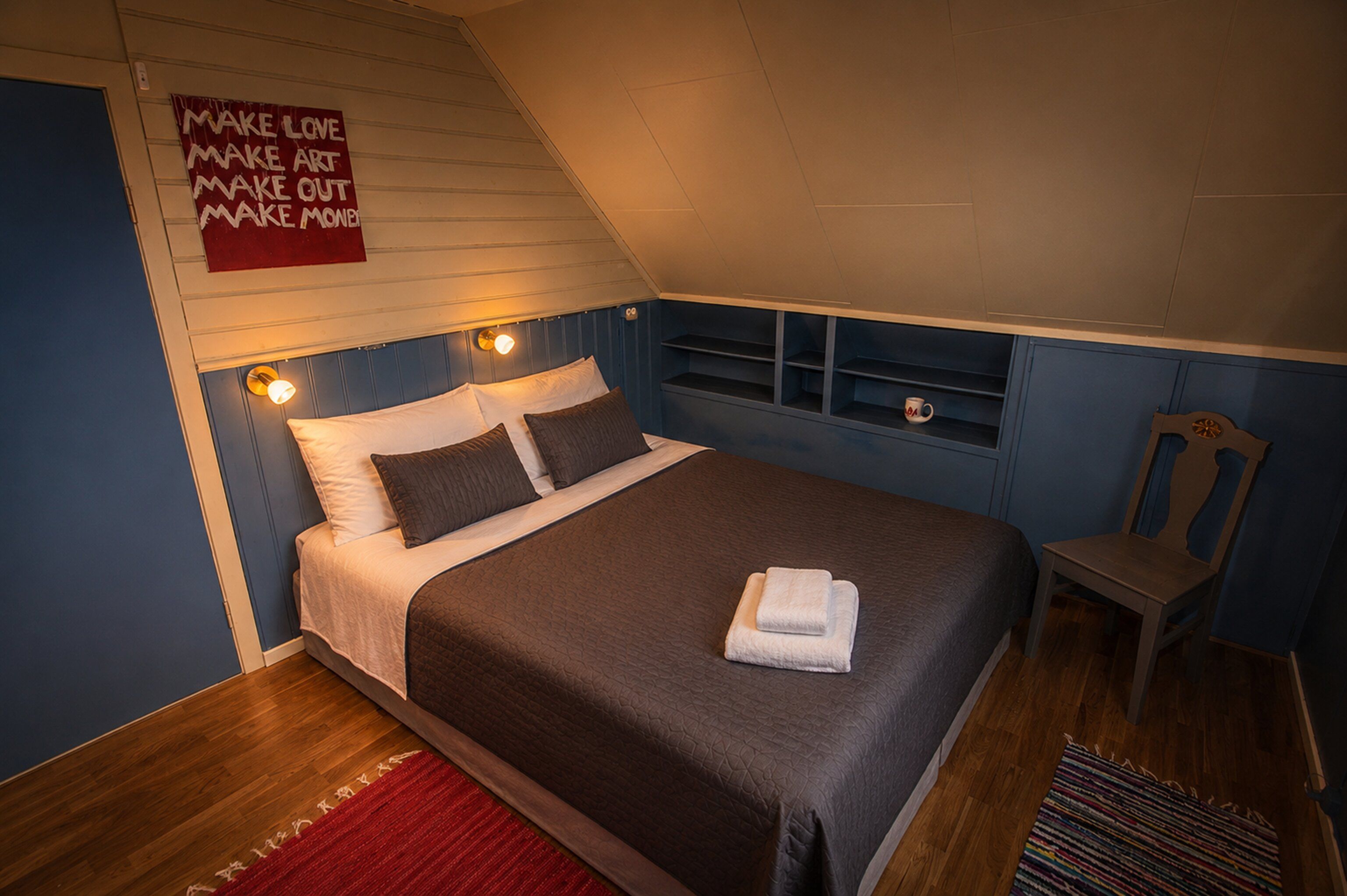 A bedroom with a bed, a chair, a shelf with a mug, and a motivational poster on the wall.