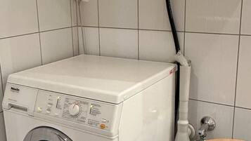 Een voorlader wasmachine in een wasserij met betegelde muren en een metalen wasmand.