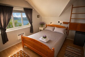 A bedroom with a wooden bed, a window with curtains, a bedside table with a lamp, and a view of mountains. - Casa Hauge Fjord View (Sandane)