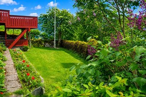 A well-maintained garden with a red wooden structure, a neatly trimmed lawn, and various flowering plants. - Casa Hauge Fjord View (Sandane)