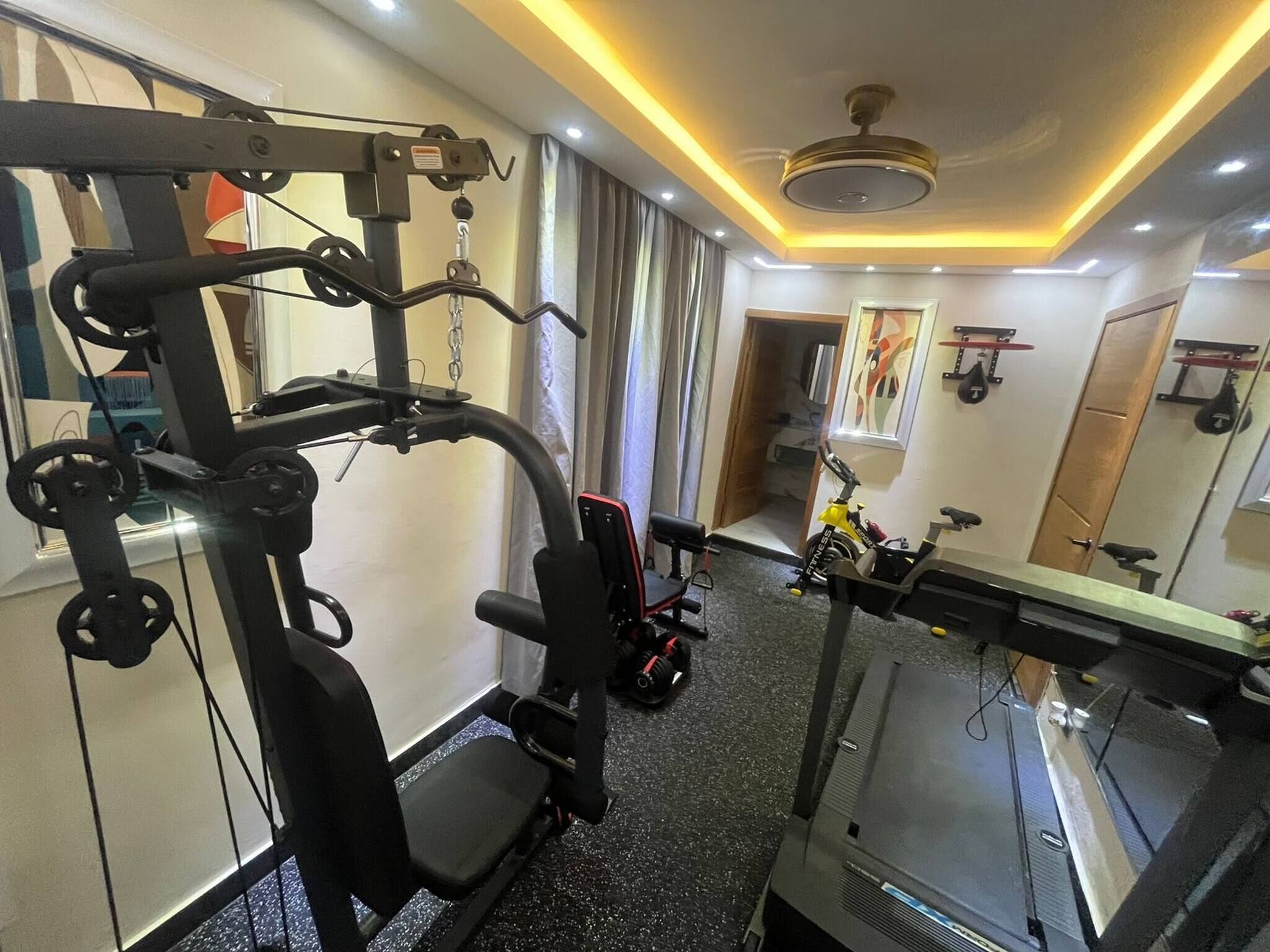 Een fitnessruimte met trainingsapparatuur, een loopband en een spiegel.