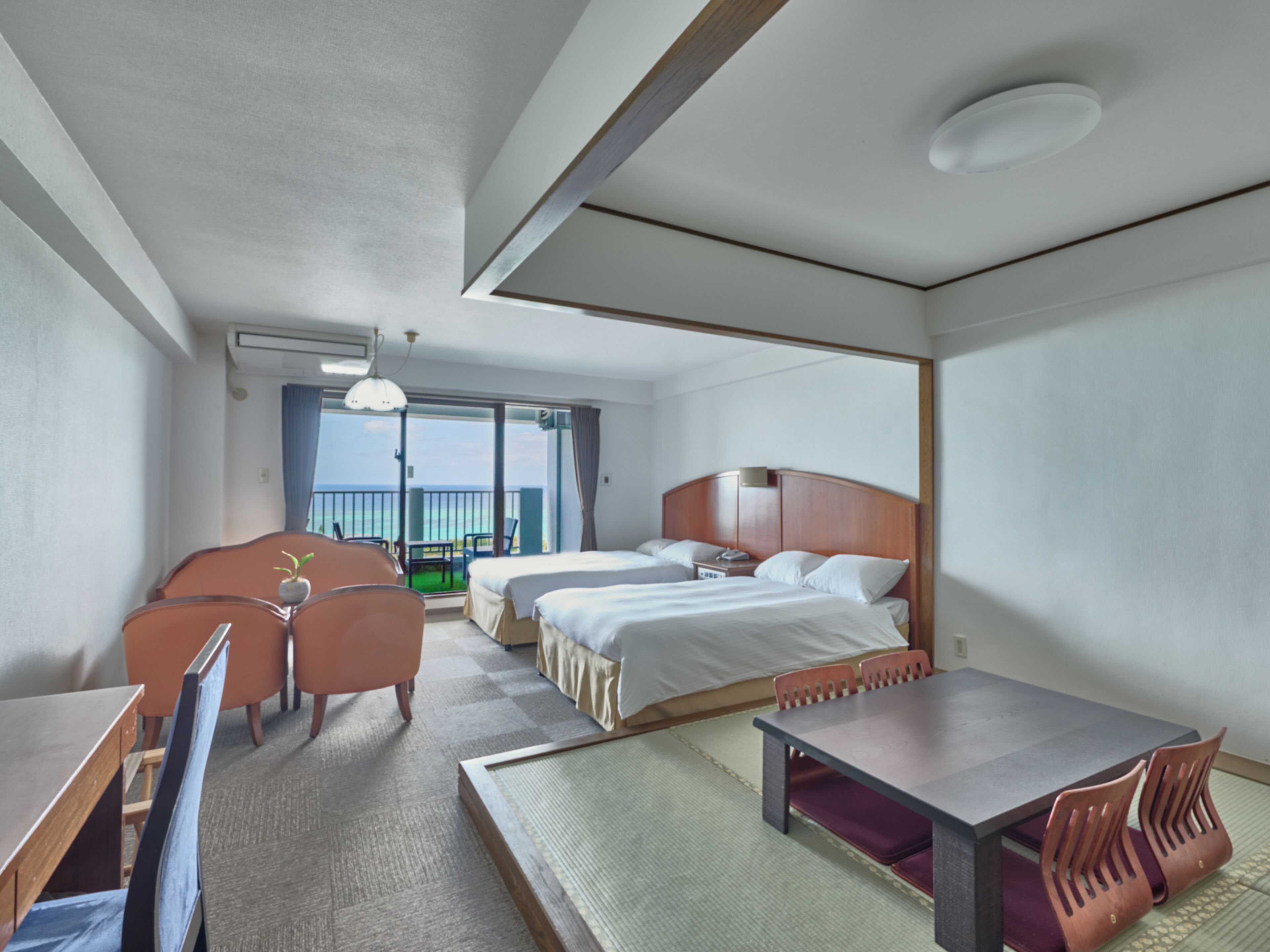 A hotel room with a bed, a desk, a chair, and a view of the sea.