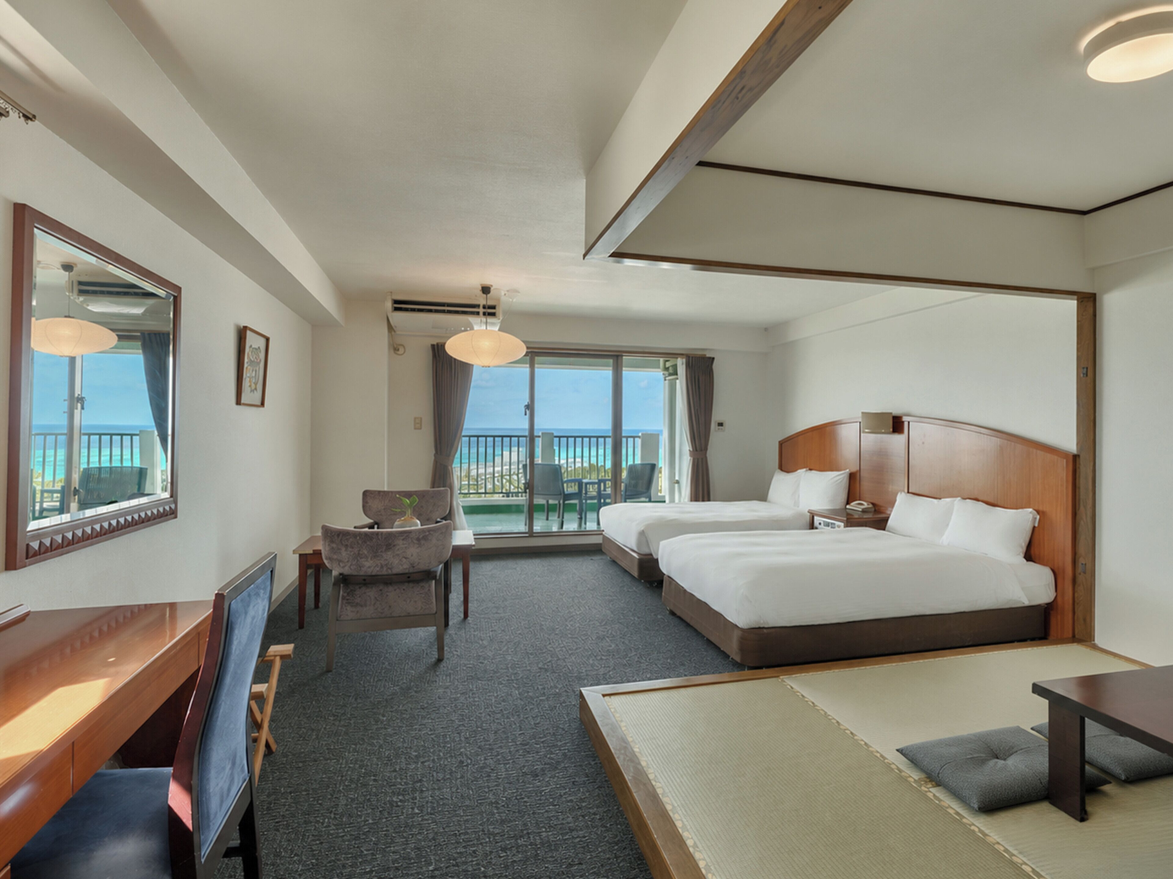 A hotel room with two beds, a desk, a chair, a TV, and a balcony with a view.