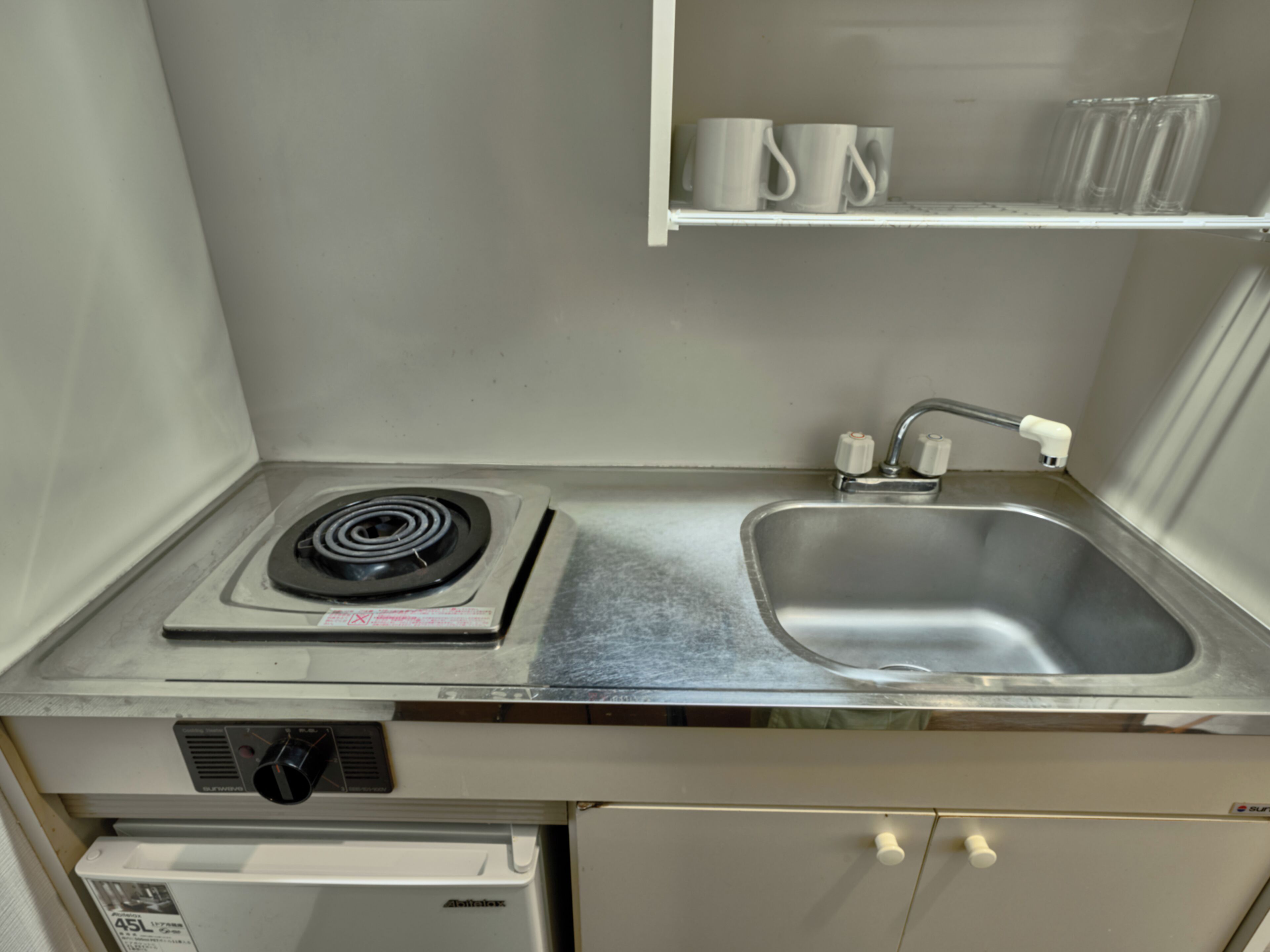 Une cuisine compacte équipée d’une cuisinière à gaz intégrée, d’un évier en acier inoxydable et d’un petit réfrigérateur.
