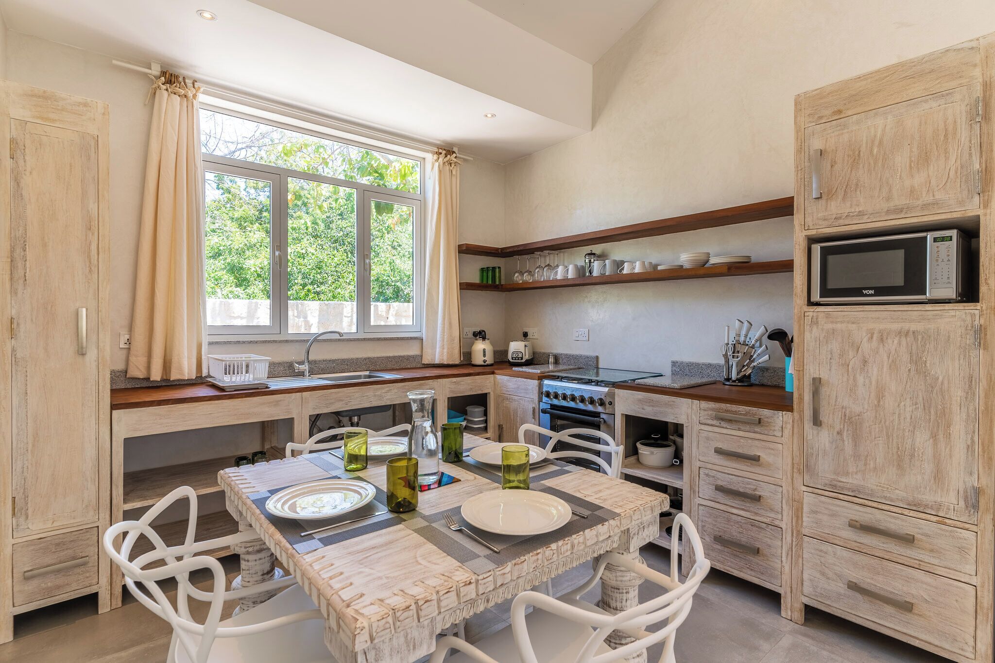 A kitchen with a dining table set for two, a microwave, and wooden cabinets.
