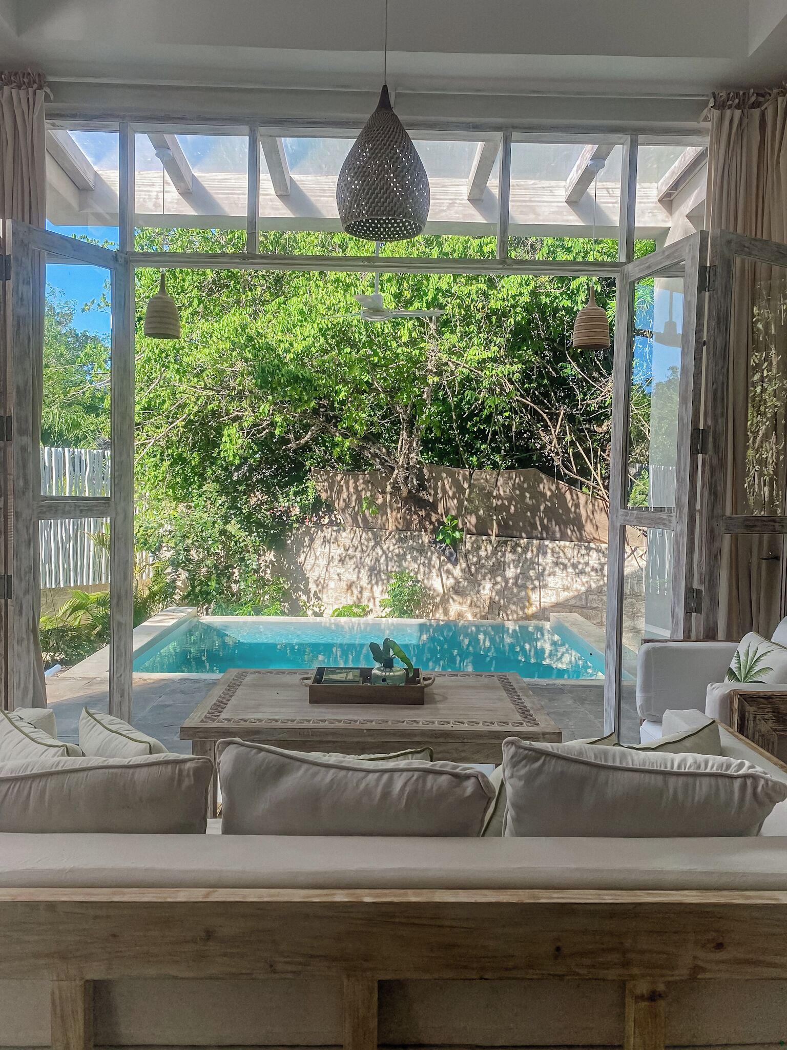 A room with a view of a swimming pool, a wooden bench, and a hanging light fixture.