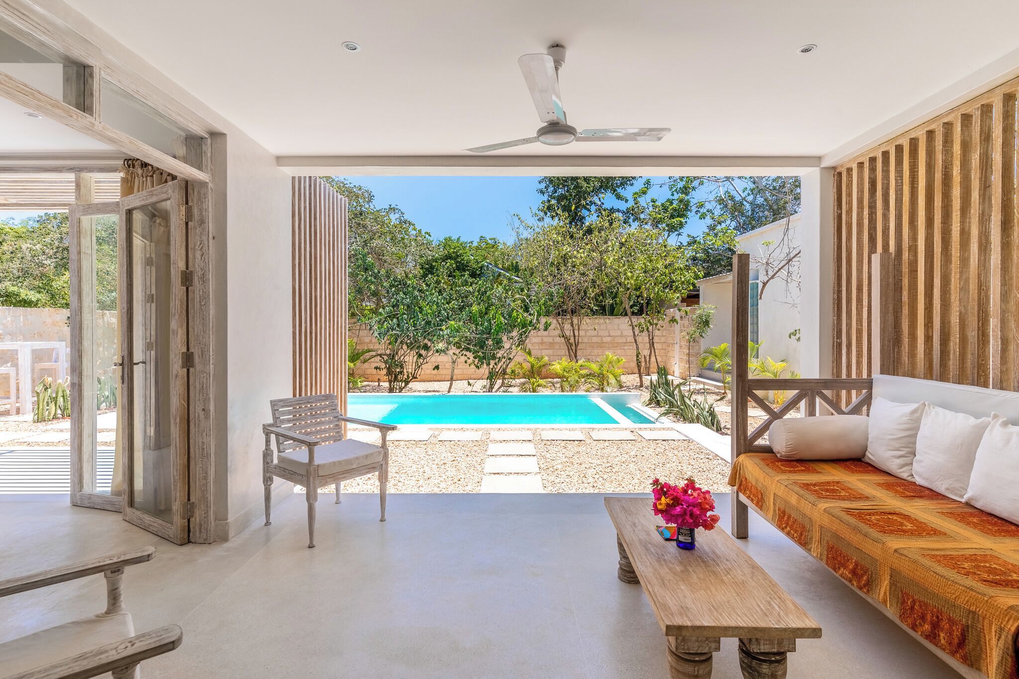 Un espacio al aire libre moderno con piscina, banco de madera, sofá y mesa con flores.