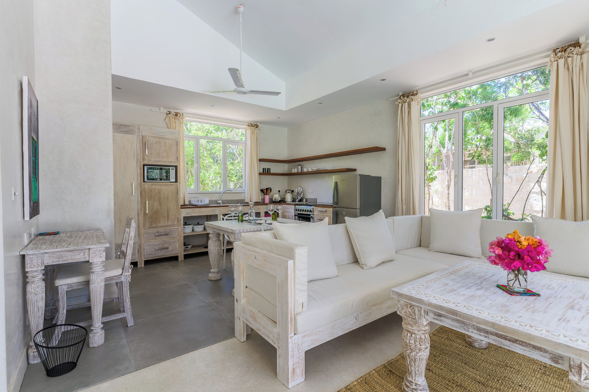 A modern kitchen with a dining area, a sofa, and a table with a vase of flowers.