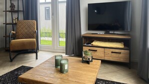 Een woonkamer met een televisie, een stoel, een houten salontafel en een plank met decoratieve objecten.