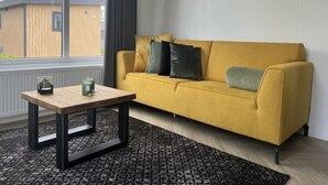 Een moderne woonkamer met een mosterdgele bank, een zwart-wit tapijt en een houten salontafel.