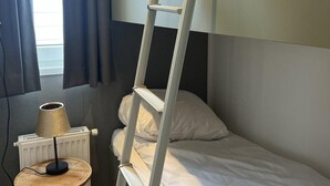 Een compacte hotelkamer met een stapelbed, een klein nachtkastje met een lamp en een radiator.