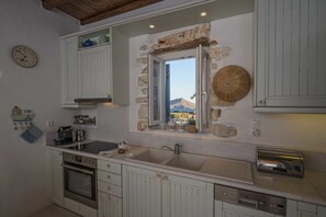A kitchen with a stone window, a clock, and a view of the mountains. - Villa Votsalo Isterni Paros (150 meters from sea) (37Q5+6F Isterni,)