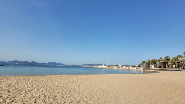 Ein weiter Sandstrand mit klarem, blauem Meer, Palmen und Bergen in der Ferne.