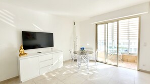 Ein modernes Wohnzimmer mit Flachbildfernseher, einem Glastisch und einer Glasschiebetür, die auf einen Balkon führt.