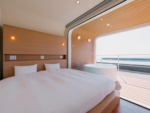 A modern bedroom with a large bed, a round bathtub, and a view of the water. - THOUSANDGARDENTARUMIZU (Tarumizu)