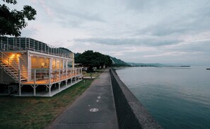 A waterfront building with a deck and outdoor seating area, adjacent to a calm body of water. - THOUSANDGARDENTARUMIZU (Tarumizu)