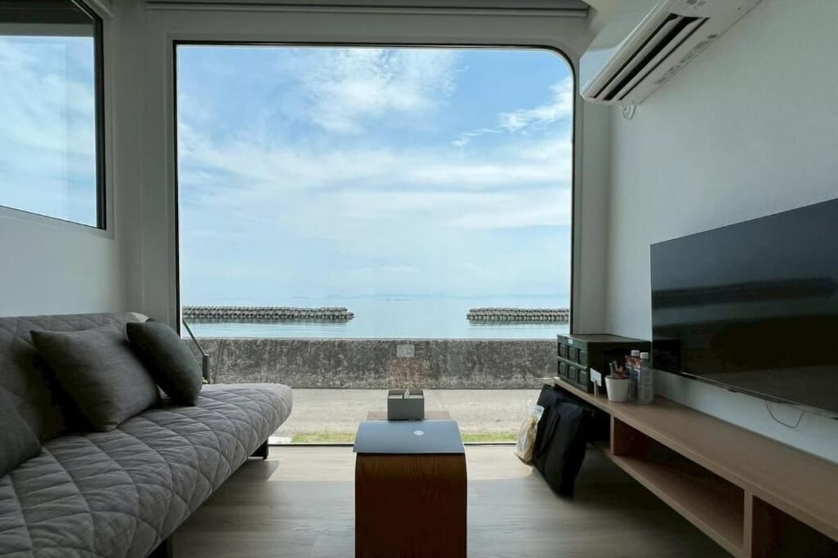 A living room with a sofa, a flat-screen TV, a coffee table, and a view of the sea.