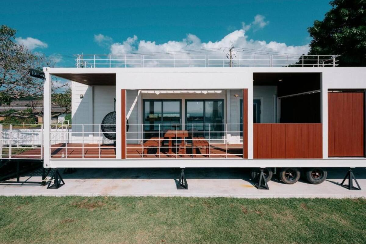 A modern, white, multi-level houseboat with a covered deck, large windows, and a dining area.