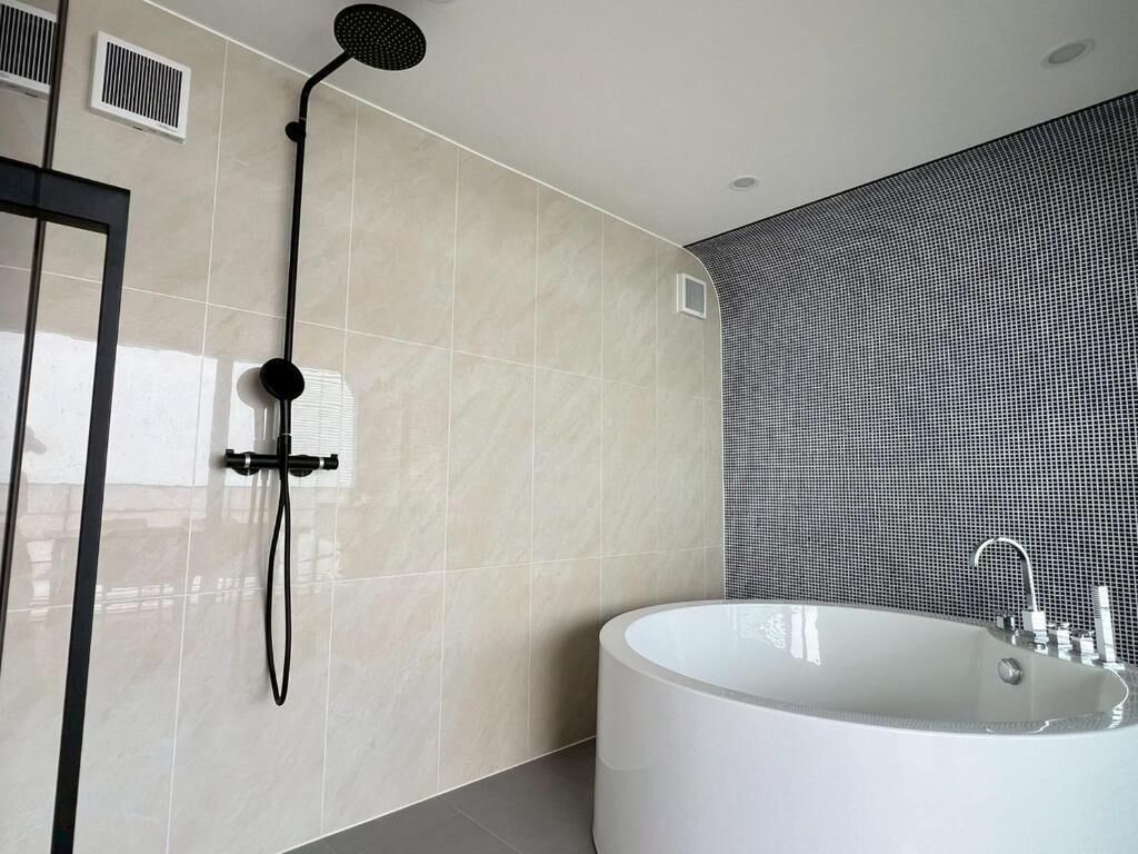 A modern bathroom with a freestanding bathtub, a showerhead, and a wall-mounted ventilation unit.