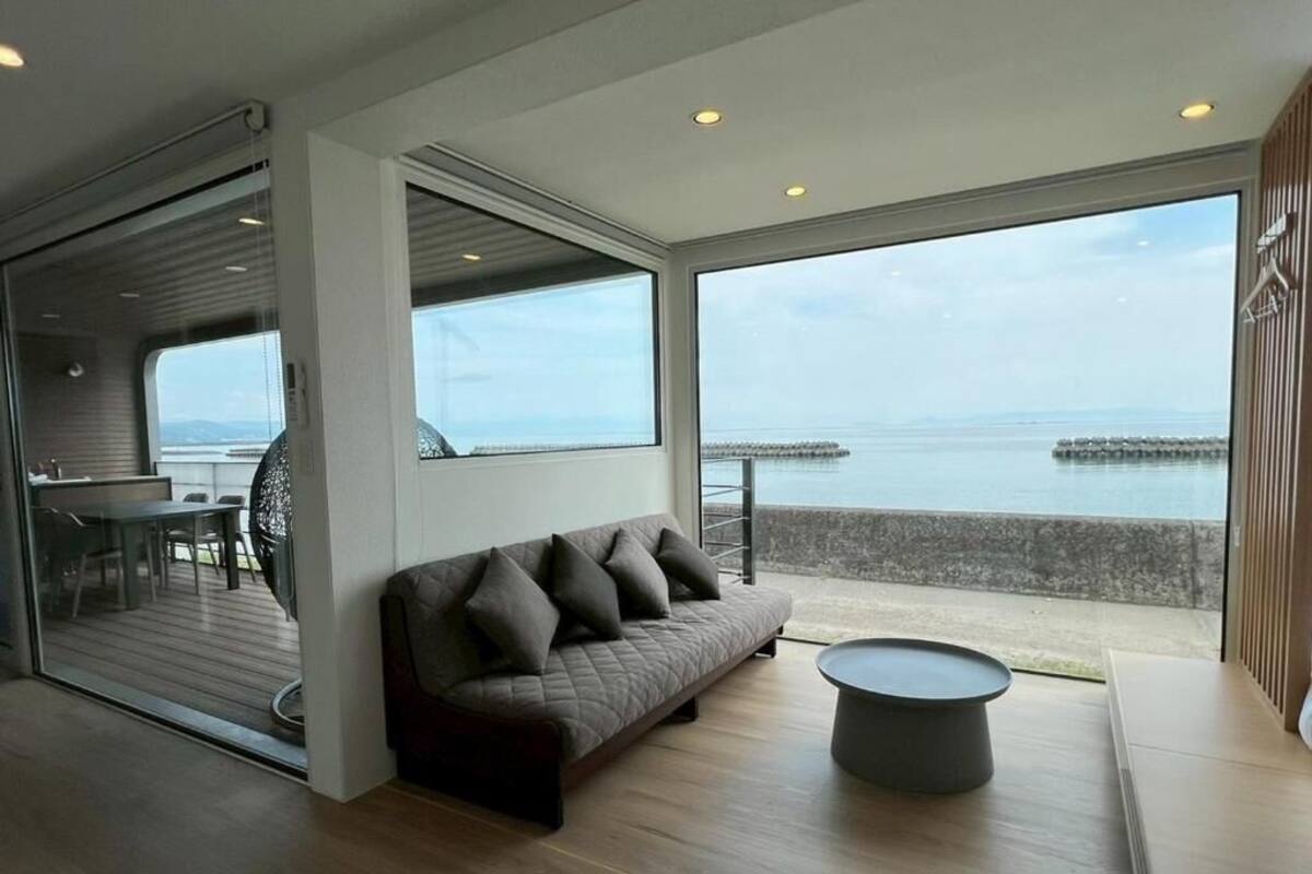 A modern living room with a sofa, a round coffee table, and large windows offering a view of the sea.