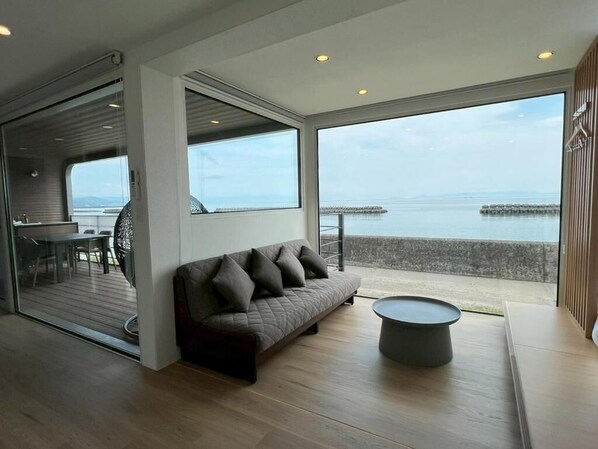 A modern living room with a sofa, a round coffee table, and large windows offering a view of the sea. - THOUSAND GARDEN TARUMIZU (Tarumizu)