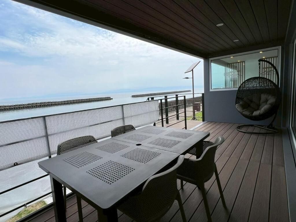 A balcony with a table and chairs, a hanging chair, and a view of the sea.