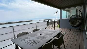A balcony with a table and chairs, a hanging chair, and a view of the sea.