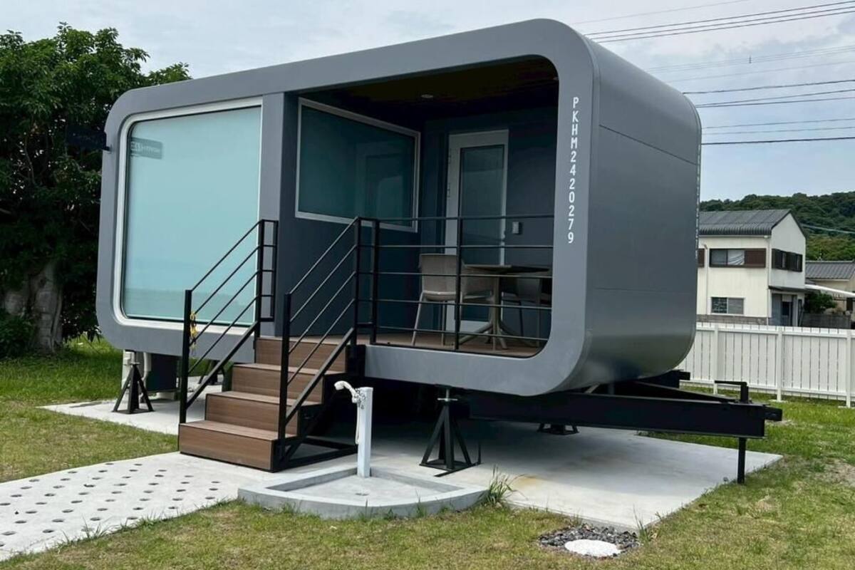A modern, compact mobile home with a large window, a staircase, and a flat roof.