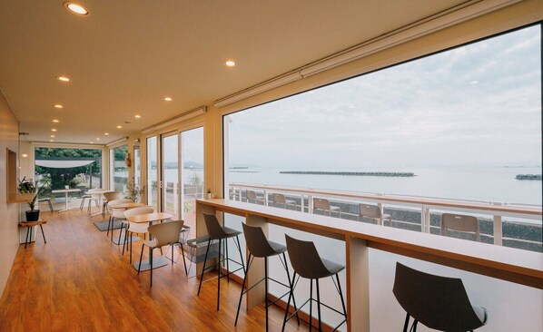 A modern interior with a long balcony overlooking a body of water, featuring a seating area with chairs and tables. - THOUSAND GARDEN TARUMIZU (Tarumizu)
