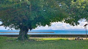 A tree-lined view of a calm body of water with a distant mountain range. - THOUSANDGARDENTARUMIZU (Tarumizu)