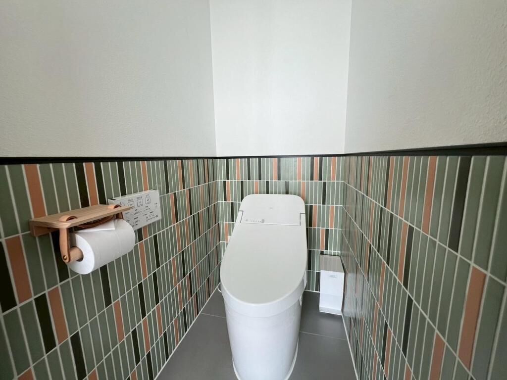 A small bathroom with a toilet, a toilet paper holder, and a wall-mounted electrical outlet.