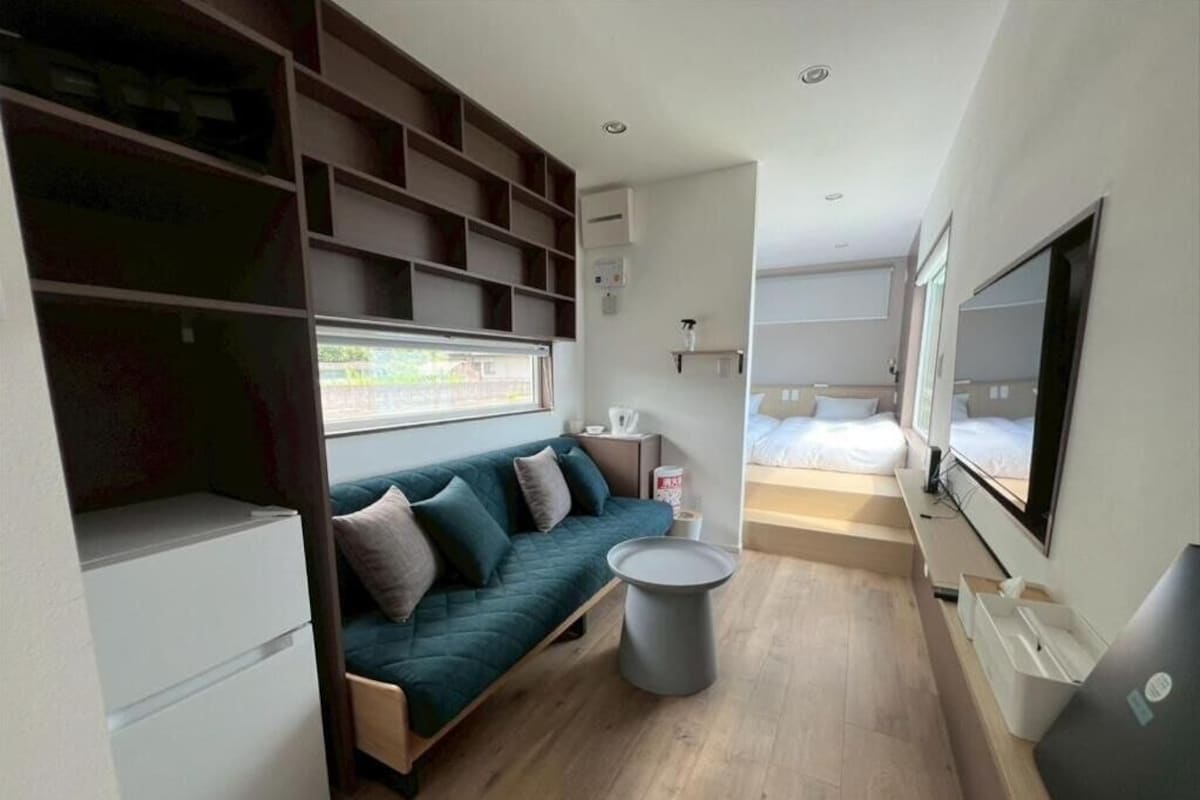 A modern hotel room with a sofa, a small round table, a TV, and a window with a view.