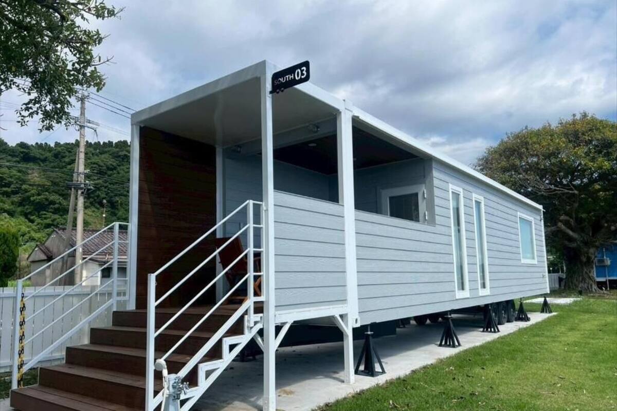 A mobile home with a covered porch, a staircase, and a sign indicating 'SOUTH 03'.
