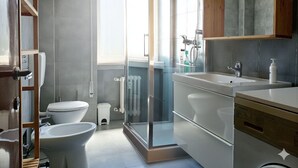 Ein modernes Badezimmer mit Duschkabine aus Glas, Toilette, Bidet und Waschbecken mit Holzschrank darüber.