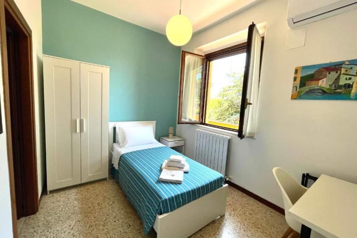 Une chambre à coucher comprenant un lit, une table de chevet, une fenêtre, un radiateur, un tableau et une armoire.