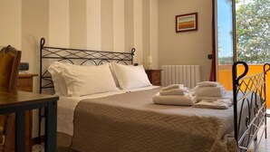 Een net opgemaakt bed met witte lakens, een nachtkastje met een lamp, en een raam met uitzicht op bomen.