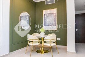 A dining area with a round table and four chairs, a vase with flowers, and two framed artworks on the wall.