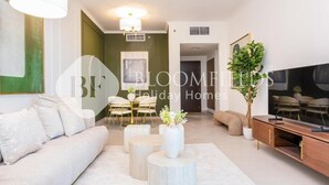 A modern living room with a sofa, round coffee tables, a TV, and a dining area with chairs and a table. - Bloomfields 2br Unique Ajwan Soul B (Abu Dhabi)