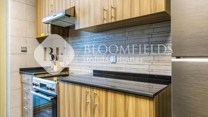 A modern kitchen with wooden cabinets, a built-in oven, and a black countertop. - Bloomfields 2br Unique Ajwan Soul B (Abu Dhabi)