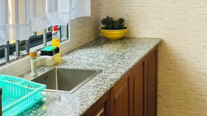 A kitchen with a granite countertop, wooden cabinets, a sink, and a window with a sheer curtain. - Liora Haven - 2BR Home That Feels Just Right (Arusha)