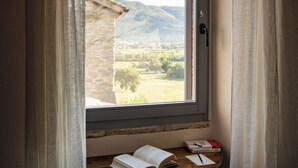 Une pièce avec une fenêtre, des rideaux, une table avec un livre et une chaise.