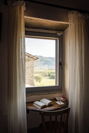 Ein Zimmer mit Fenster, Vorhängen, einem Tisch mit einem Buch und einem Stuhl.