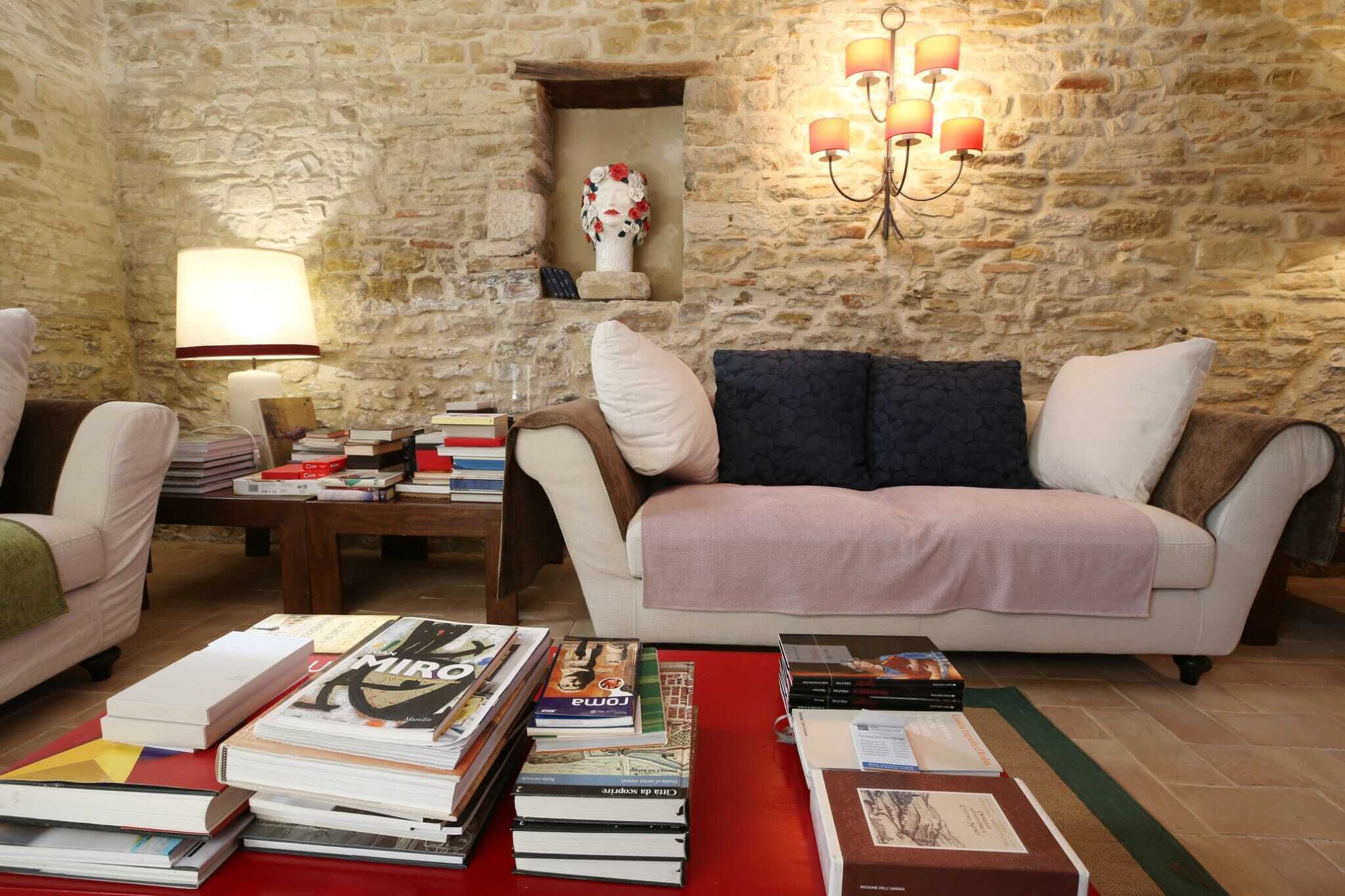 Un salón acogedor con pared de piedra, chimenea, sofá, una mesa de centro con libros y una lámpara.
