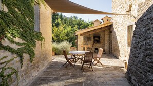 Une terrasse extérieure avec un sol en pierre, une table et des chaises, et une pergola en bois offrant de l’ombre.