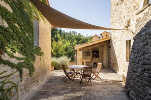 Eine Terrasse im Freien mit Steinboden, einem Tisch und Stühlen sowie einer Holzpergola, die Schatten spendet.