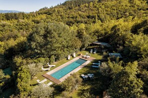 Ein rechteckiger Pool, umgeben von Liegestühlen und einer Holzterrasse, eingebettet in eine üppige, bewaldete Landschaft.