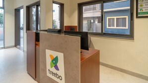 A reception desk with a logo, a window with blinds, and a door leading outside. - Treebo Hub (Indore)