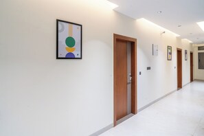 A hallway with doors, a framed abstract artwork, and recessed ceiling lighting. - Treebo Hub (Indore)