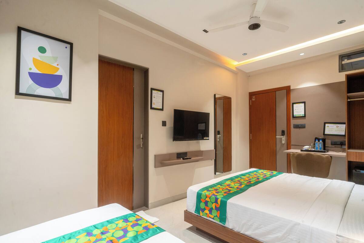 A hotel room with two beds, a TV, a desk with a computer, and a ceiling fan.