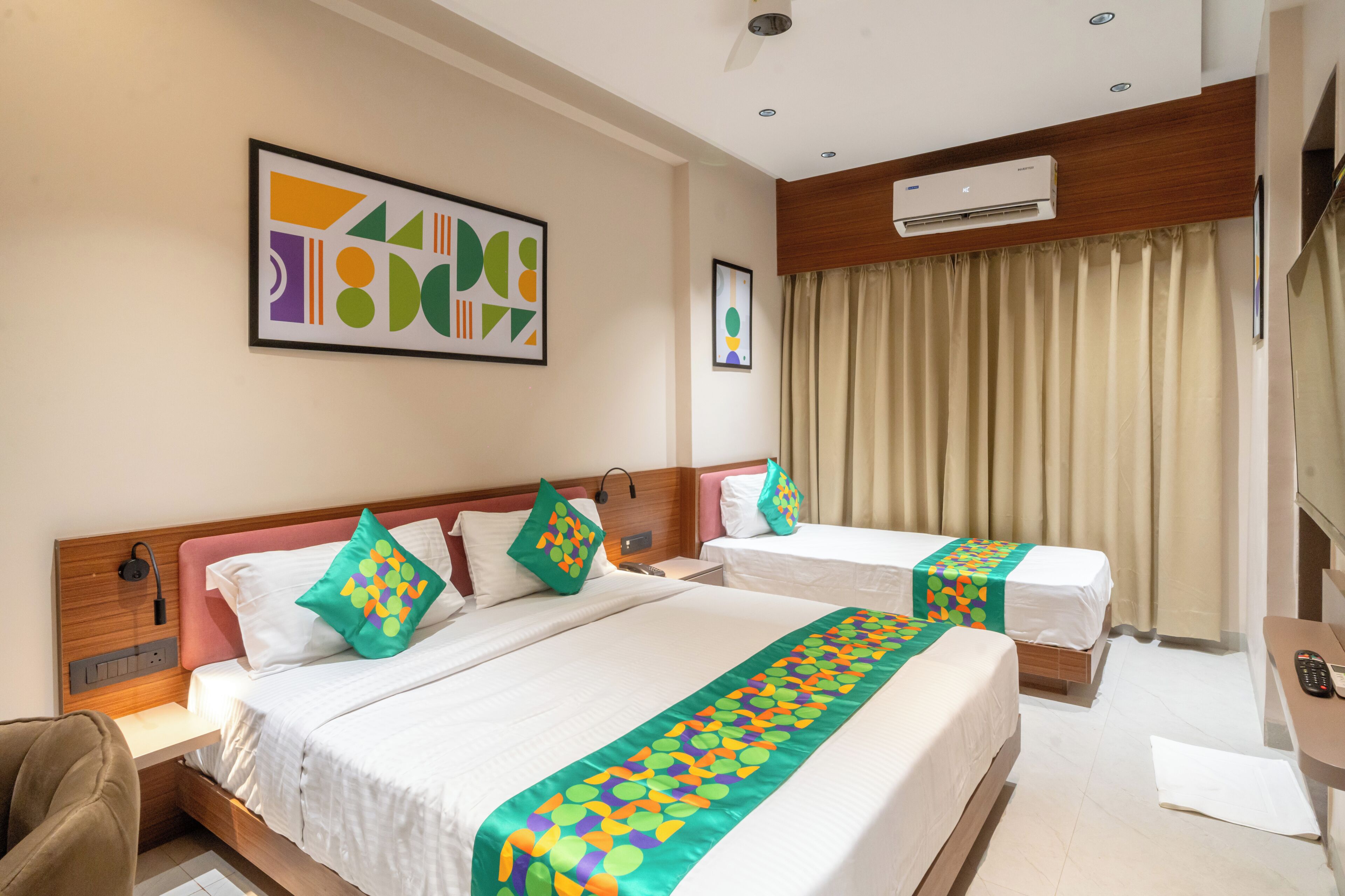 A hotel room with two beds, a desk, a chair, an air conditioning unit, and a large window with curtains.